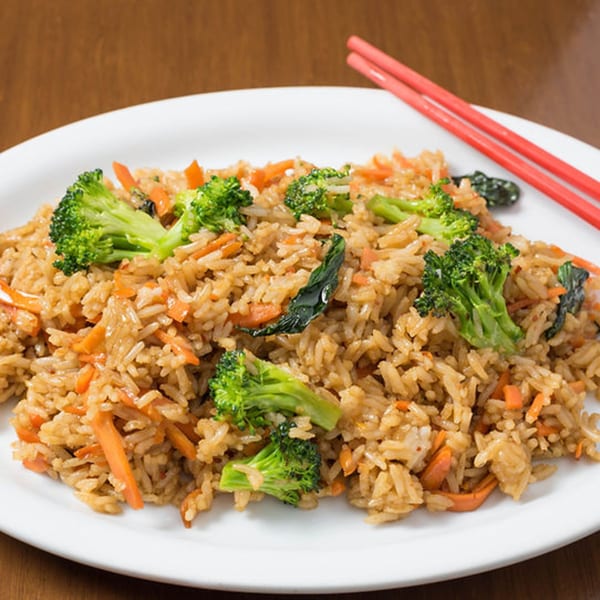 Bon Mi's fried rice with broccoli, carrots, and green leaves, served with red chopsticks.
