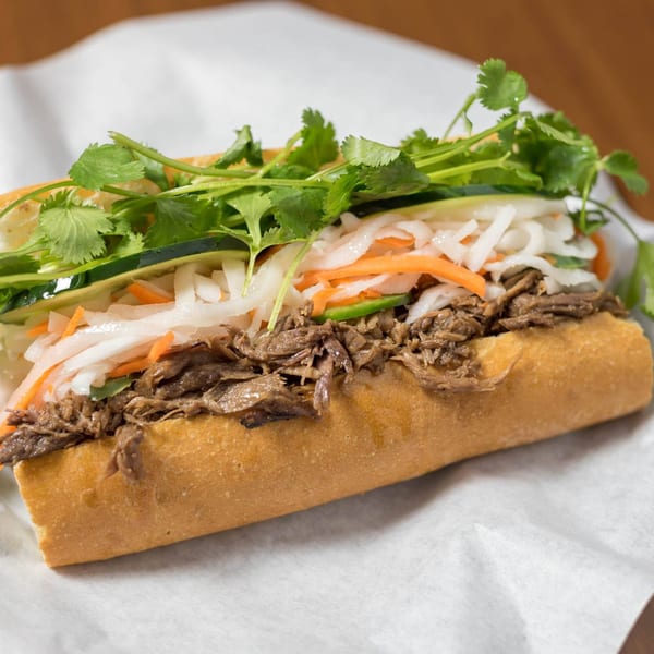 A Bon Mi Vietnamese sandwich with shredded meat, pickled vegetables, and fresh cilantro on a baguette.