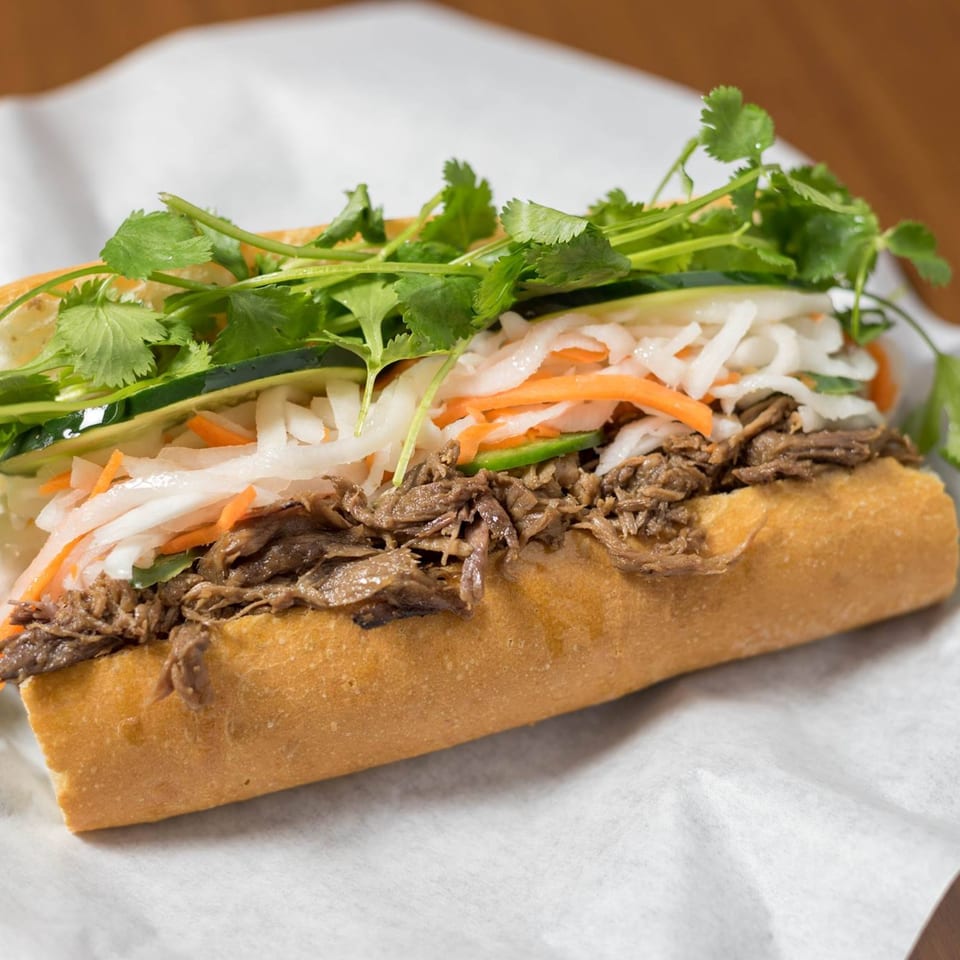 A Bon Mi Vietnamese sandwich with shredded meat, pickled vegetables, and fresh cilantro on a baguette.