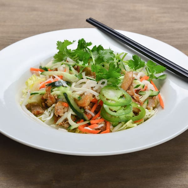 Vietnamese salad with chicken, mixed vegetables, cilantro, and sliced jalapeños, with chopsticks.