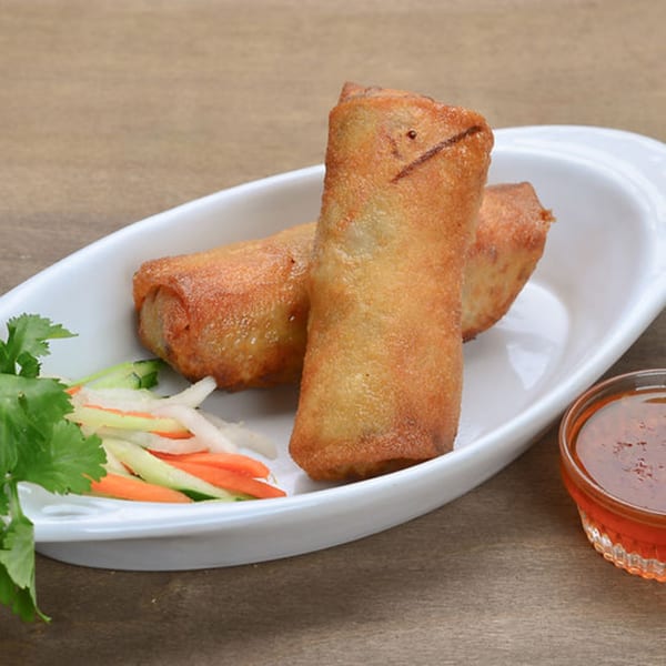 Two crispy Vietnamese spring rolls on a white plate with pickled vegetables and a dipping sauce.