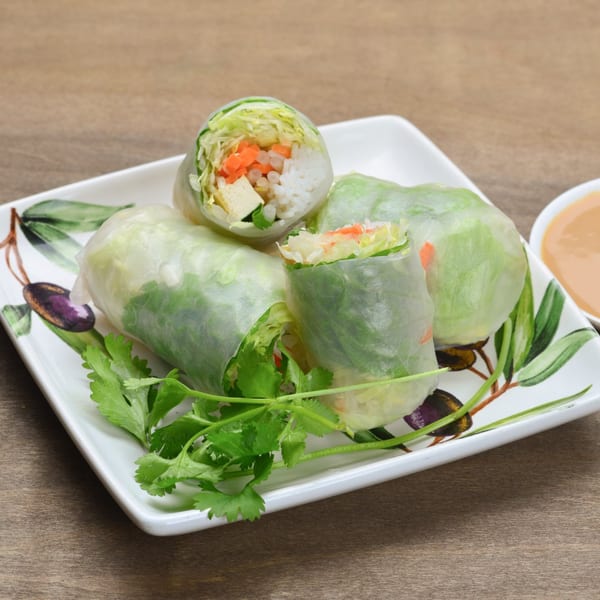 Fresh Vietnamese spring rolls with vegetables, tofu, and rice noodles, garnished with cilantro on a white plate.