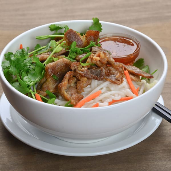 Bon Mi's Vietnamese noodle bowl with grilled meat, fresh cilantro, carrots, and a side of sauce.