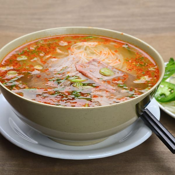 Spicy Vietnamese pho with noodles, meat, and herbs, served with chopsticks and fresh garnishes.