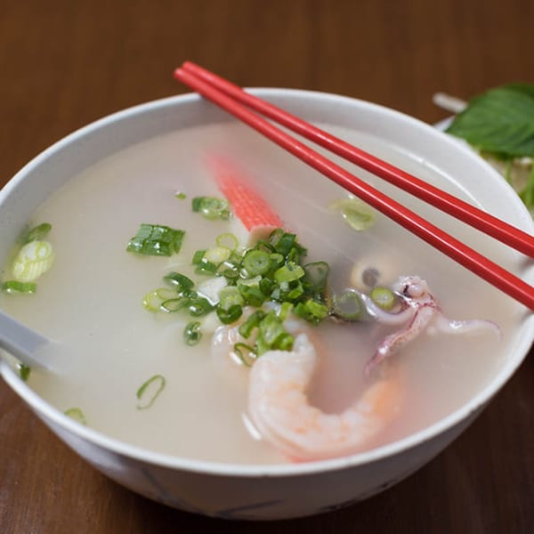 Vietnamese seafood pho with shrimp, squid, and green onions in a white bowl with red chopsticks.