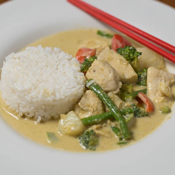 Bon Mi's yellow curry with chicken, broccoli, green beans, and rice, served with red chopsticks.